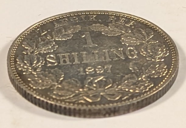 SOUTH AFRICA, Zuid Afrikaansche Republik ~ 1897 ~ Shilling ~ Bust of Paul Kruger left ~ Value divides date in wreath, Z. AFRIK. REP. above. ~ Y-4, KM-5 ~ Nice unc., a few marks